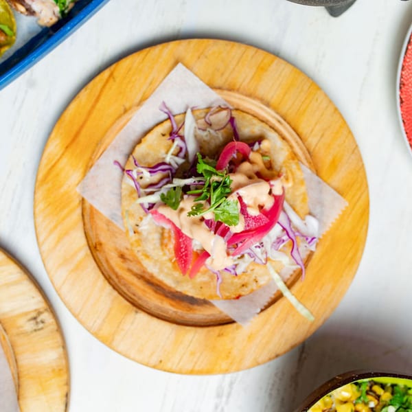Overhead view of a single Taco City DC taco with red cabbage, cilantro, and sauce on a wooden plate.