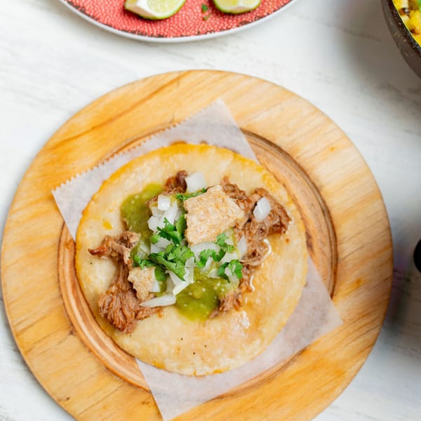 A Taco City DC carnitas taco with green salsa, onions, and cilantro on a wooden plate.