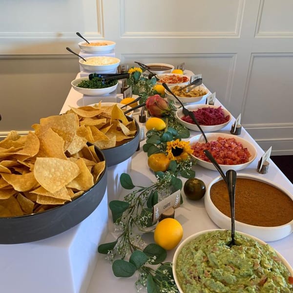 A buffet table with bowls of tortilla chips, guacamole, salsa, and other Mexican toppings.