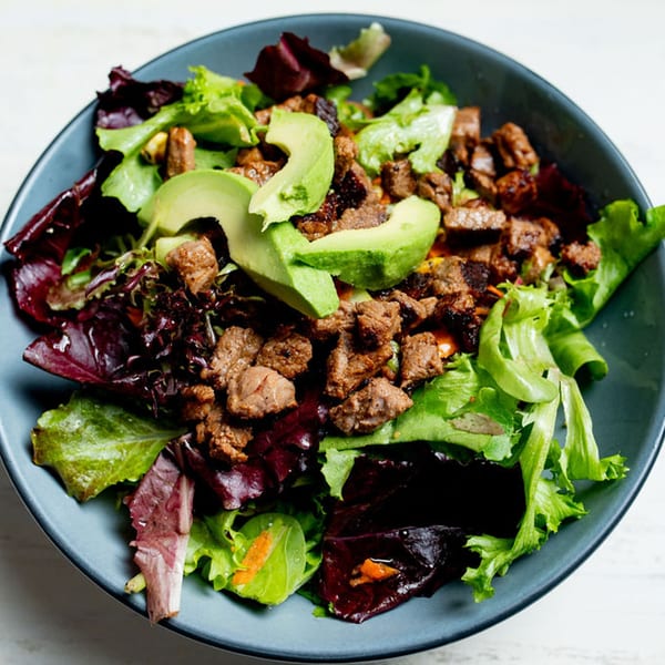 Taco City DC's vibrant salad with mixed greens, steak, and sliced avocado in a dark bowl.