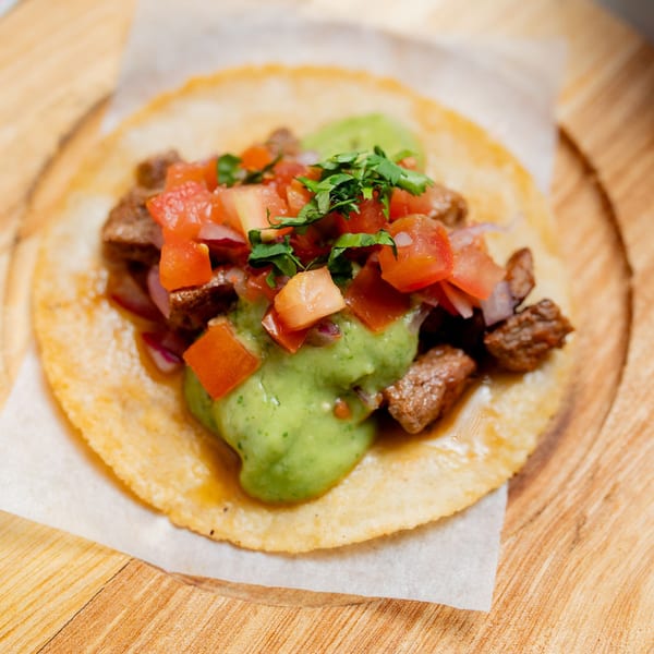 A Taco City DC carne asada taco with guacamole, pico de gallo, and cilantro on a wooden board.