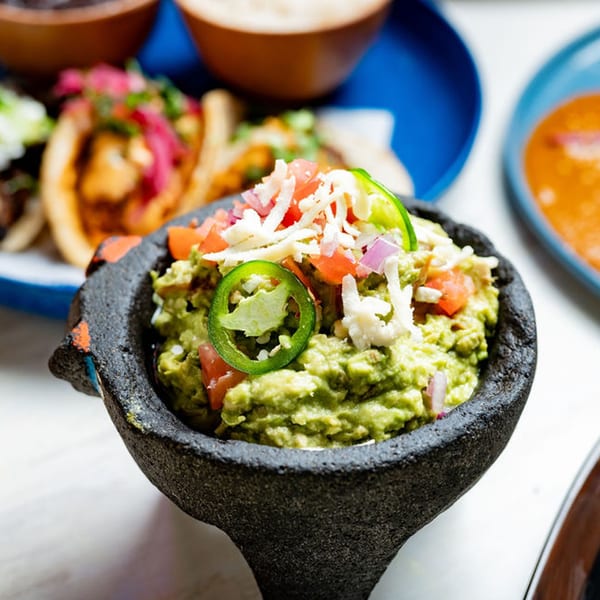 A close-up of a molcajete filled with guacamole, topped with cheese, tomatoes, onions, and jalapeños.