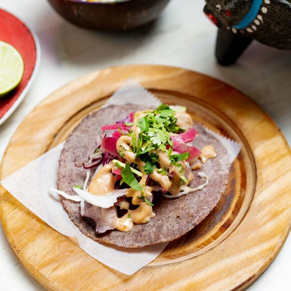 A Taco City DC taco with purple tortilla, red onions, cilantro, and sauce on a wooden plate.