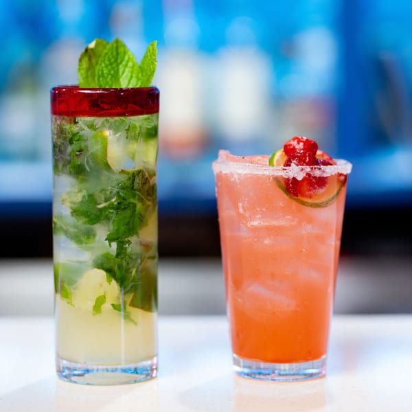 Two refreshing cocktails, a mojito with mint and a pink margarita with berries, on a white bar.