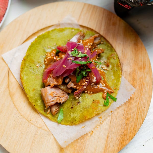 A vibrant green taco from Taco City DC, topped with meat, red pickled onions, and sesame seeds.