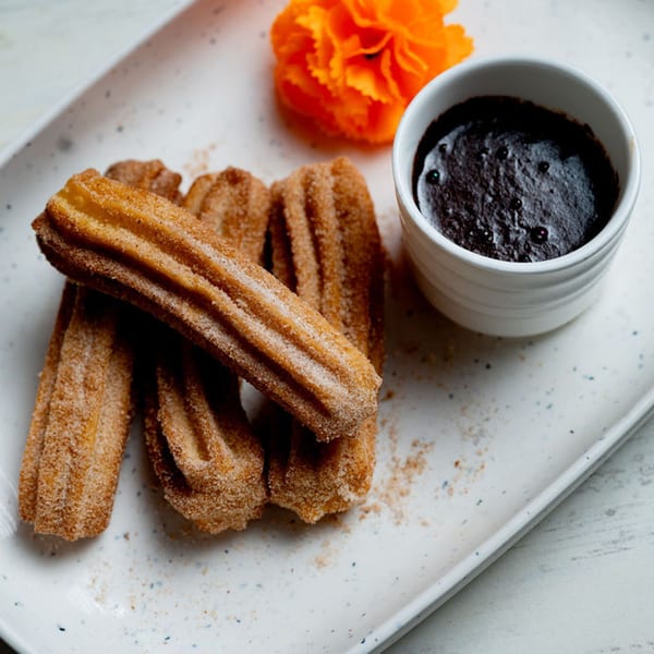 Churros with cinnamon sugar and a side of chocolate dipping sauce, garnished with an orange flower.