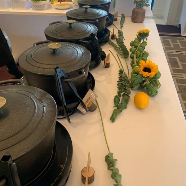 A buffet line with several black cast iron pots, tongs, and decorative sunflowers with greenery.